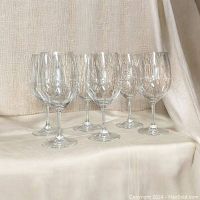 Set of six clear red wine glasses with visible stems and flat round bases, arranged on a cloth surface.