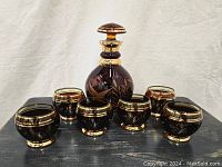 Full set view of decanter with stopper centered among six matching glasses showing overall appearance and size.