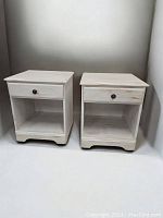Pair of whitewashed pine end tables with black metal drawer pulls, front view showing drawers and open shelves with decorative base molding.