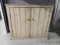 Front view of vintage whitewash pine cupboard showing double paneled doors and wooden knob handles.