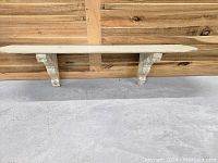 Front view of large whitewashed pine shelf supported by two carved corbels, placed against wooden wall.