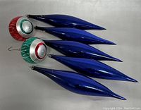 Seven vintage Christmas tree ornaments displayed outside the box including five blue icicle-style and two round red and green ones.