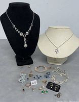 Front view of necklaces on display busts with assorted jewelry laid below including rings, earrings, bracelets, and pendants.