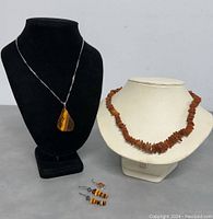 Two necklaces and two pairs of earrings displayed on black and white bust forms and lying on grey surface.