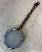 Full view of the 37-inch Beltone 5-string banjo with wooden neck, metal rim, and clear banjo head on tiled floor.