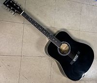 Black Huntington acoustic guitar full body on tiled floor
