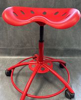 Front view of red swivel stool with visible seat contour and footrest ring on caster wheels.