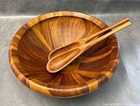 Photo of large teak wooden bowl with two wooden spoons resting inside, showing rich wood grain and joinery details.
