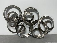 Full view of interconnected concentric metal circles with a swirled texture on a plain white wall.