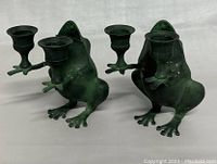Two antique brass frog candleholders, each holding two cup-shaped candle holders, showing patina and minor wear.
