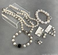 Photo shows two vintage pearl necklaces, two pearl bracelets with silver accents including one with a black bead, and three pairs of pearl drop earrings on a gray surface.