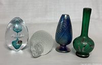 Photo showing four items side by side: clear signed Czechoslovakia crystal paperweight with blue elements inside, clear glass hedgehog paperweight, blue swirled glass vase, tall green glass vase with silver designs.
