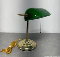 Side view of vintage brass base and green lamp shade with yellow power cord coiled beside it.