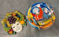 Ceramic Bacchus mask and wall hanging plate side by side showing colorful details and condition.