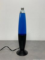 Front view of vintage lava lamp with blue wax inside clear container and black base with power cord laid out