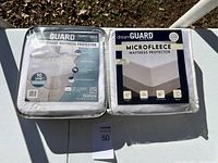 Two Dream Guard mattress protectors side by side on a white table outdoors, showing packaging.