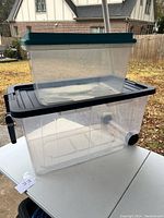 Two stacked clear plastic storage totes with teal lids placed on an outdoor table, showing full size and shape.