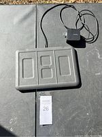 Full view of the black Magnifo 4 device charging mat and attached power adapter on outdoor surface with lot tag.