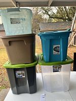 Five storage totes stacked and displayed on a table outdoors. Different colors and lids shown.