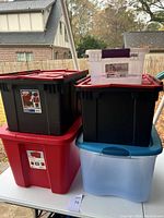 Photo of five stacked plastic storage totes in various colors and sizes on a white table outdoors