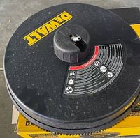 Top view of black circular surface cleaner with DeWalt yellow logo and safety instruction decal on top knob.
