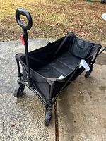 Side angle of the black folding pull cart showing the fabric storage area and front wheels.