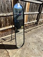 Full length black metal framed mirror in standing position outdoors showing reflective surface and frame details.