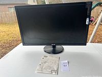 Front view of ASUS VP278QG monitor with user manual placed in front, outdoors on a table.