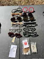 Image showing 12 pairs of glasses including sunglasses and eyeglasses laid out on a table, along with two small packaged accessory items.