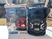 Front view of the Technical Pro SPARK12B speaker next to its product box showing product details and branding.