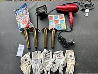 Overview photo showing all items on black table including golf gloves, metal legs, hair dryer, floodlight, toys, and battery charger.