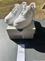 Pair of white Nike Air Force 1 shoes displayed on top of original box, size label visible showing size 8.5, outside shot with natural light highlighting rhinestone swoosh detail.