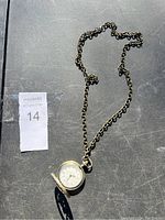Photo of the pocket watch attached to its chain lying on a black surface with natural light highlighting the details.