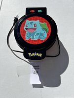 Closed waffle maker showing top lid with Bulbasaur graphic and Pokemon logo, power cord visible.