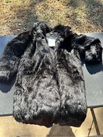 Full view of black faux fur polyester coat laid flat showing texture and length.