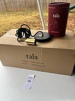 Overview of the Pottery Barn Tala pendant light components including brass socket, black cord, black ceiling mount, and Tala packaging on top of a cardboard box, with outdoor background.