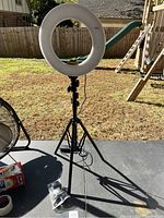 Full view of the ring light mounted on a black adjustable tripod stand outside, showing condition and power cord.