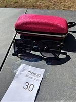 Photo of black Tom Ford sunglasses placed in front of red protective case on a black table outdoors, showing overall lot content.