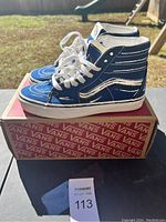 Front and side angle view of blue Vans high-top shoes on Vans branded shoebox outdoors.