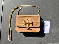 Wooden purse with gold-tone chain strap and large logo on front flap.