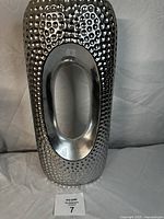 Front view of silver decorative vase with hammered texture and oval cutout in the center.