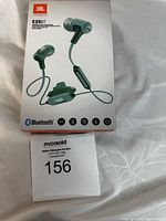 Front photo of sealed box showing JBL E25BT wireless in-ear headphones in green color with Bluetooth and feature icons.