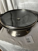 Full view of the Breville electric wok showing round shape, glass lid, and stainless steel base with Breville logo.