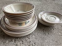 Stack of plates and bowls showing floral design and decorative rims, used condition with some visible marks.