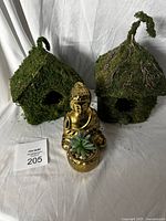 Photo showing two moss-covered straw houses and golden Buddha statue with artificial plant in front.