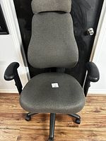 Front view of grey upholstered office desk chair showing cushioned seat, adjustable black armrests, and five-wheel base.