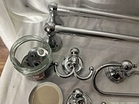 Set of chrome bathroom accessories displayed on bed including two double towel bars, multiple hooks, a round towel ring, and a toilet paper holder, all with classic style finials.