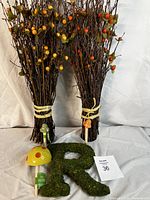 Two bundles of decorative twigs with orange and green berries, two mushroom figurines on sticks, and a moss-covered letter 'R'
