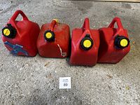 Four used red plastic jerry cans/fuel containers with yellow caps placed on concrete floor, showing overall lot contents and condition.