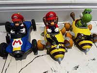 Front view of all three remote control cars showing Mario in blue kart, Mario in yellow bee kart, and Yoshi in green bee kart.